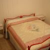 Letto matrimoniale con copriletto rosa e bianco, due comodini bianchi con lampade.