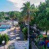 Piscina con ombrelloni, palme e area giochi, insegna 