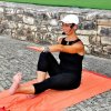 Persona fa yoga all'aperto su un tappeto arancione.